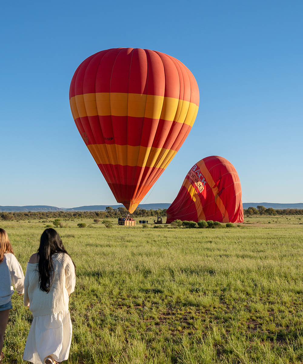 Two women approaching hot air balloons in the outback. 