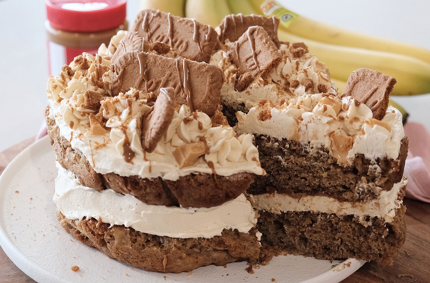 A two-tier banana Biscoff cake layered with cream cheese icing and topped with Biscoff cookies, white chocolate chunks, and Biscoff drizzle. 