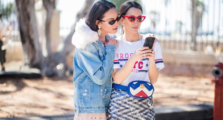 Two women stand close while gazing at a mobile phone.