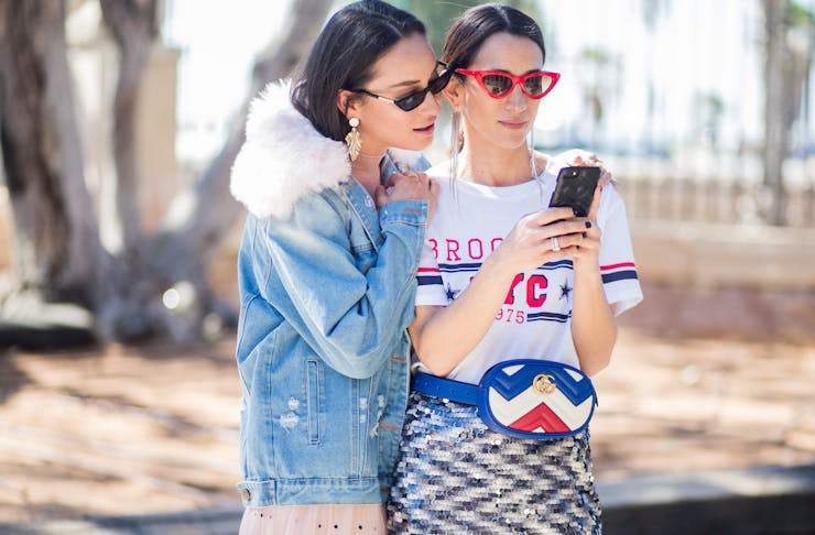 Two women stand close while gazing at a mobile phone.