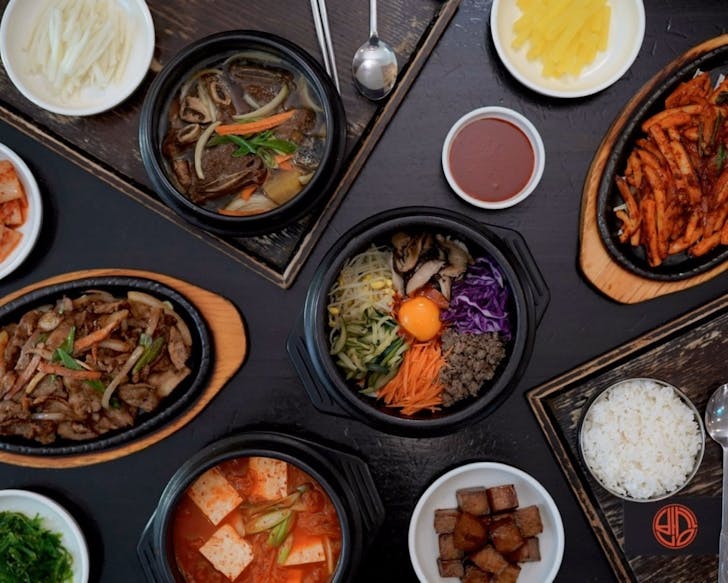 A table filled with different Korean dishes, including bibimbap, sizzling grilled beef and side dishes.