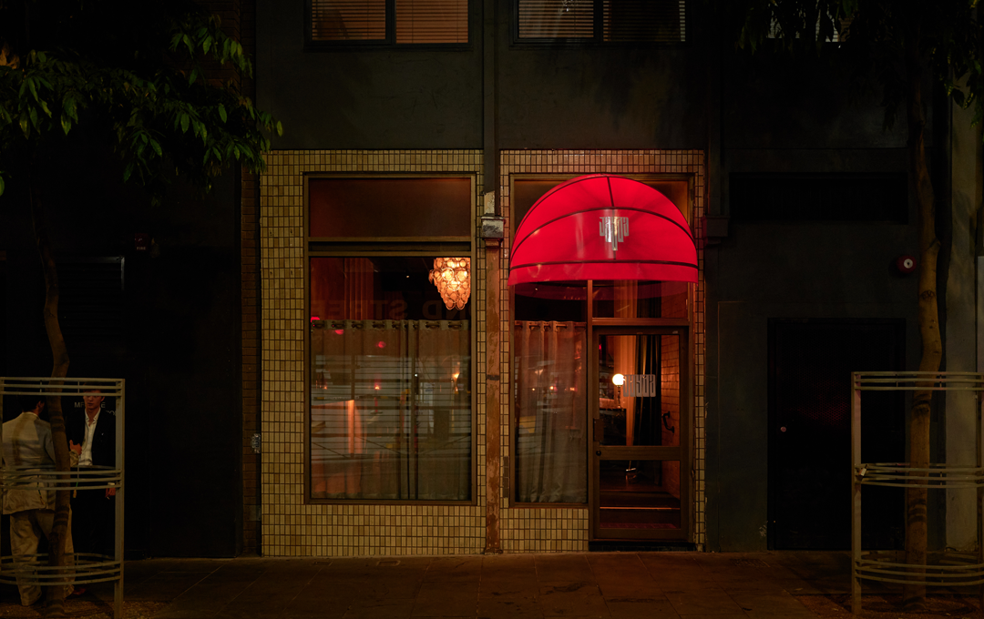 A shopfront with a large red awning lit up at night, one of the best cocktail bars Melbourne. 