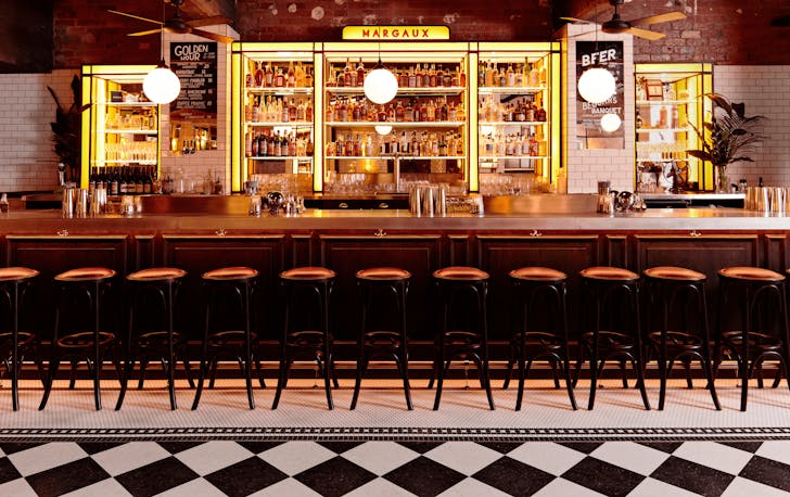 A checkered floor and yellow-lit sign at one of the best cbd bars Melbourne. 