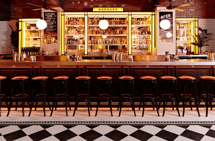 A bar with checkered floors, stools and bottles on a shelf.