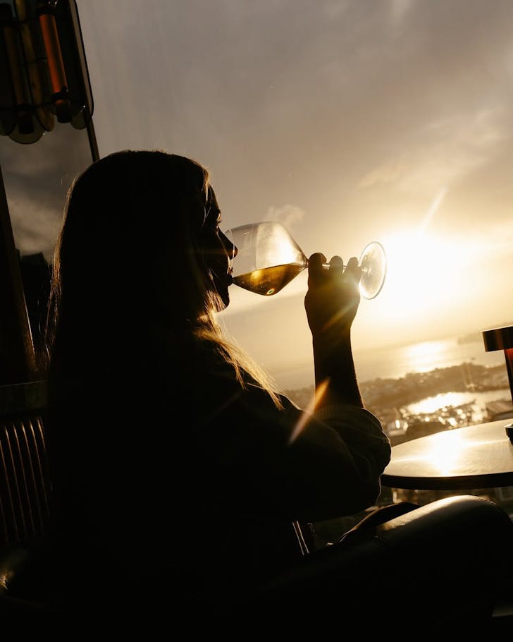 A person enjoys a glass of wine in the sunset at Bar Albert. 