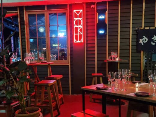 Tall bar tables and stools with a red neon light in the background that says 'Yoku' in stylised writing.