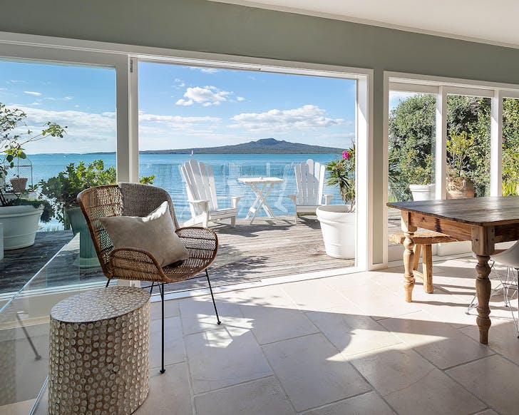 A well appointed room looks out onto a sunny deck with Rangitoto in the distance.