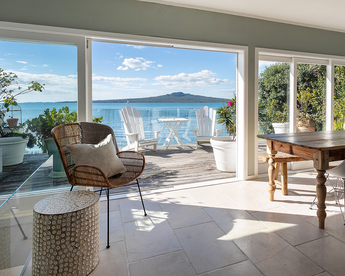 A well appointed room looks out onto a sunny deck with Rangitoto in the distance.