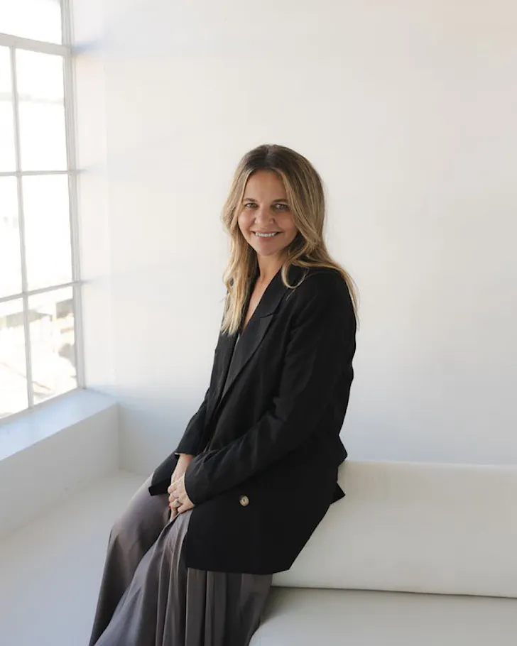Belinda Carr sits on the edge of a couch and smiles. 