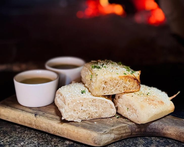 Dough balls sit on a wooden chopping board, accompanied by two bowls of condiments.