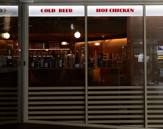 The shop front of Belles Chicken with a light sign that reads 'Cold Beer' and 'Hot Chicken'. 