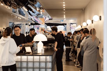 A busy cafe with people standing at a bar and a large overhead mirror.