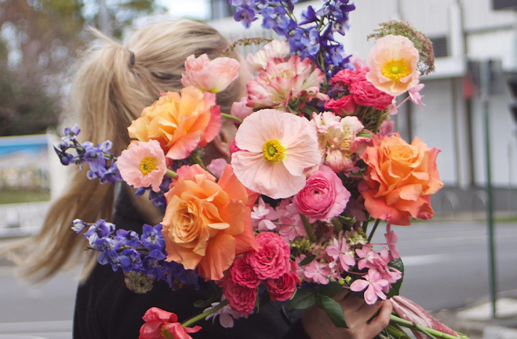 A woman holding a bunch of unwrapped flowers in pinks and purples from Bespoke Botanics, a flower delivery Melbourne has on offer