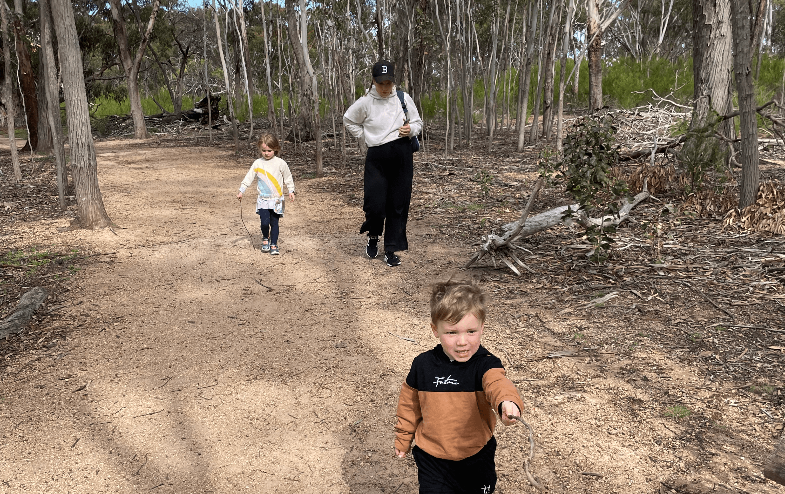 A person and two kids walking in the bush. 
