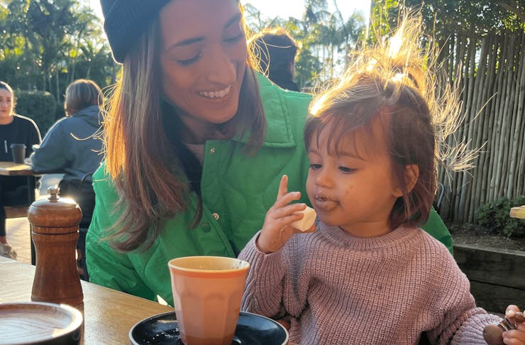 A person smiling with a small child drinking a baby cino. 