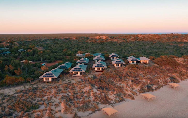 a cluster of cabins on the beach at sunset.