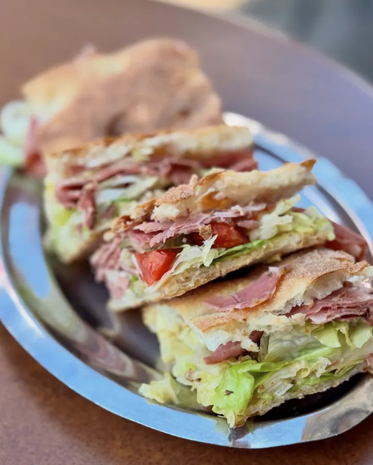 Best coffee spots in Rome at Bar del Cappuccino with thickly stacked pastrami sandwiches on a silver platter