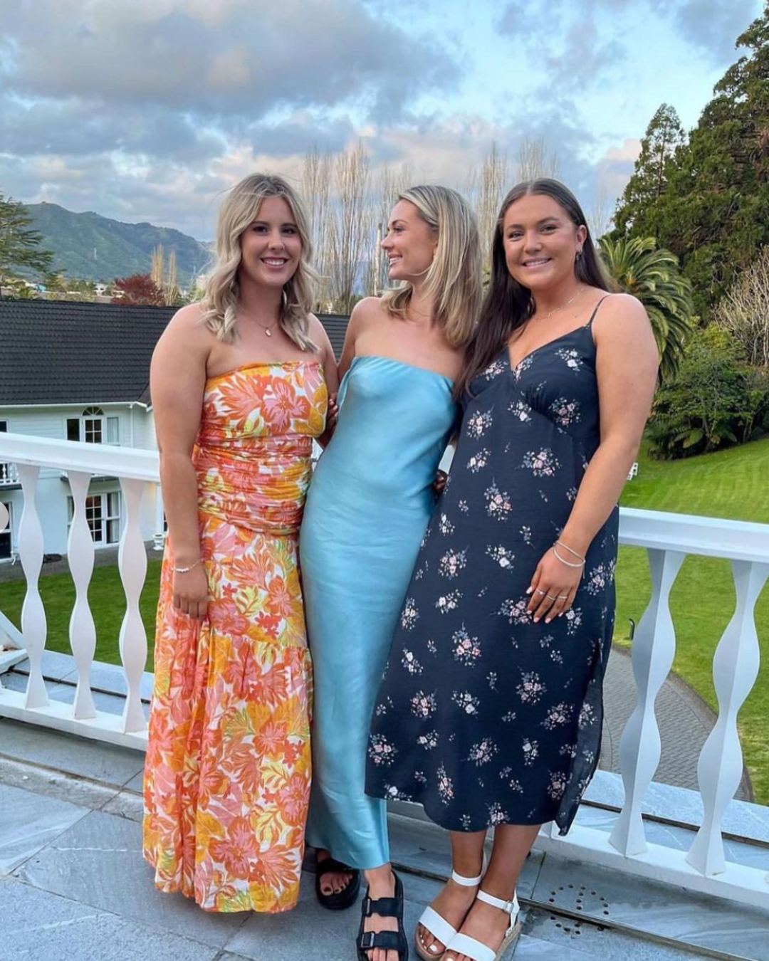 Three women pose wearing different dresses.