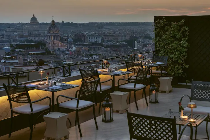Best rooftop hotels in Rome at Hotel Hassler with its lit-up rooftop dining area looking out over the Rome skyline