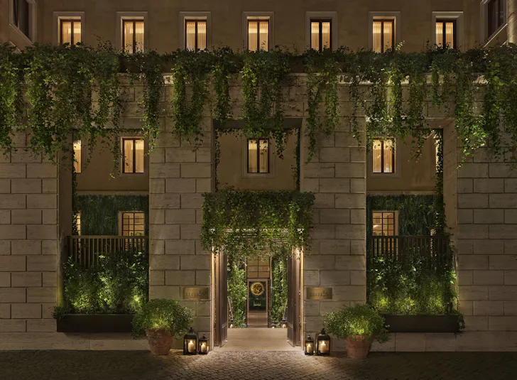The entrance of a luxury hotel in Rome lit up at night with hanging green vines, plants and lanterns