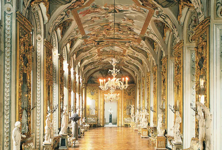 Ornate gilded gallery inside Galleria Doria Pamphilj in Rome with chandeliers, frescoed ceilings and classical sculptures