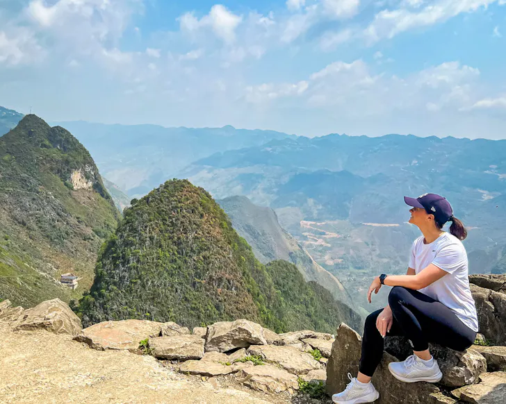 A woman sits on the edge of a path, overlooking the cliff faces of a scenic walk.