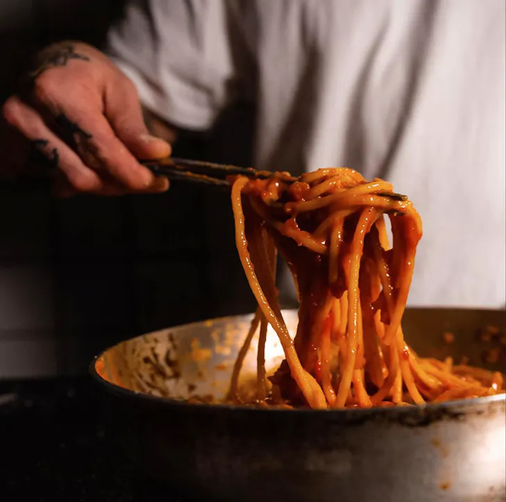 Best pasta in Rome at Trecca with someone serving pasta in a tomato based sauce from a fry pan