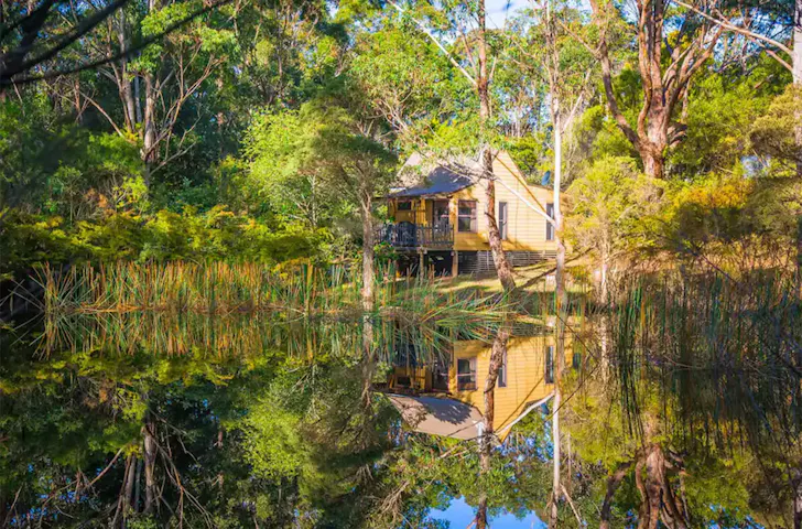 A view of the yellow Billabong Cottage Airbnb from across the water, it's one of the best pet-friendly stays near Sydney