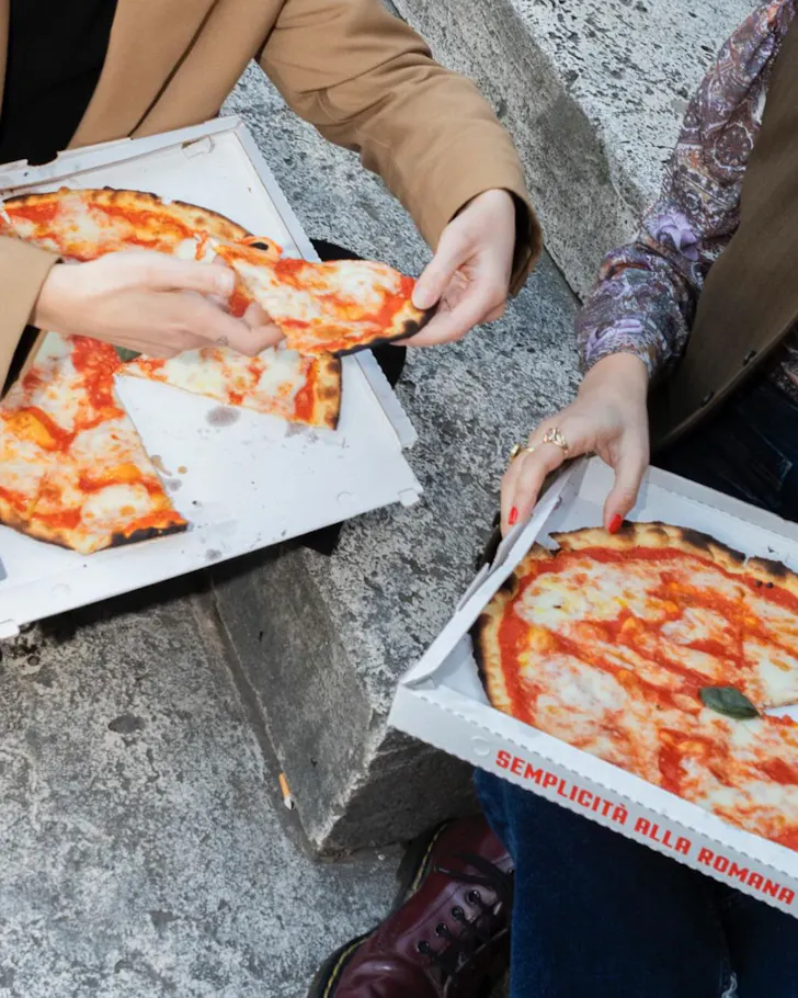 Best pizza in Rome at L'Elementare with two people holding pizza boxes, sitting on stairs