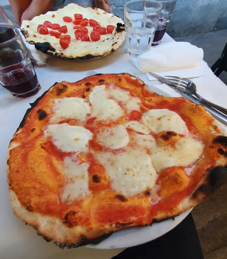The best pizza in Rome at Pizzeria Remo with two large, rustic style pizzas covered in cheese and tumblers of wine