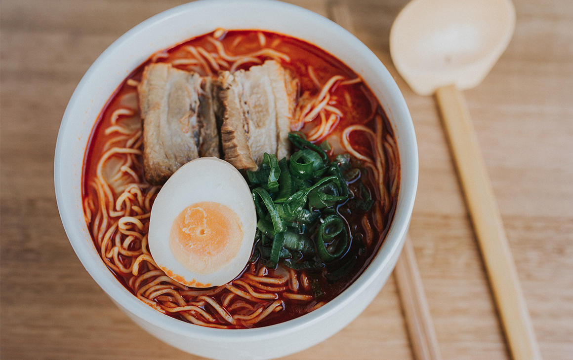 A bowl of red-coloured Japanese ramen, topped with pork.