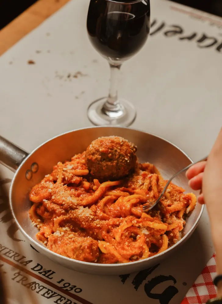 Best restaurants in Rome at Nannarella with a bowl of tonnarelli pasta and meatballs and a glass of red wine