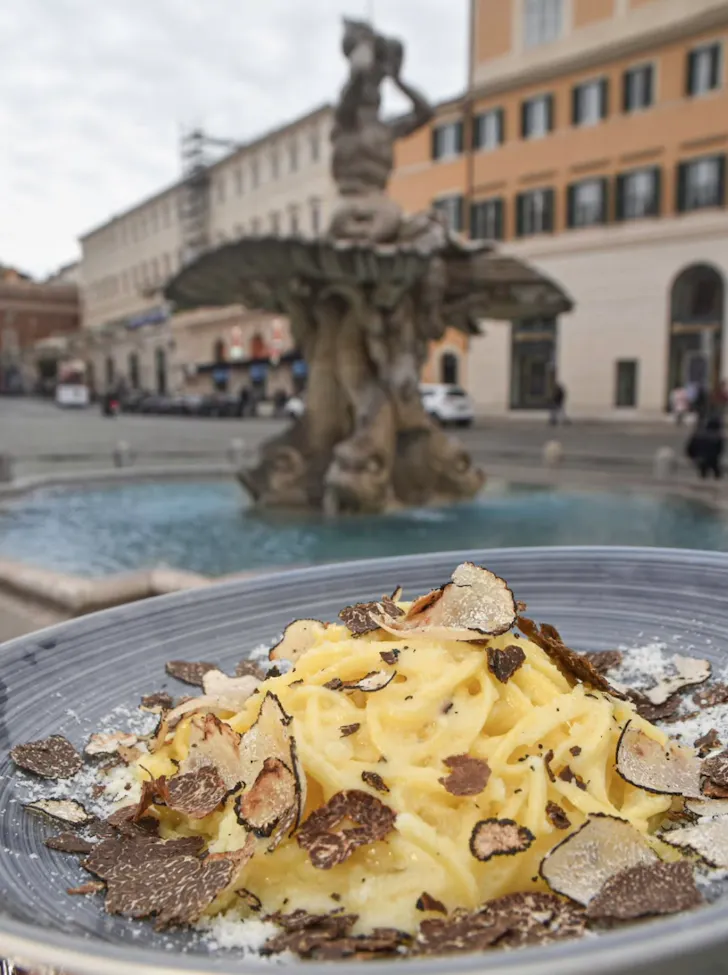 Best restaurants in Rome at Osteria Barberini with a bowl of pasta covered in truffles set against a Roman fountain background