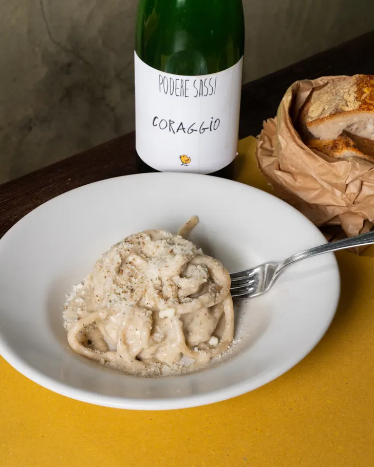 Best restaurants in Rome at Trattoria Pennestri with a bowl of creamy pasta, basket of bread and bottle of wine