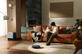 Man on couch with a dog as robot vacuum works on the carpet