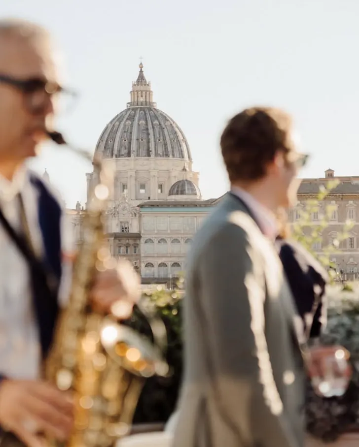 Best rooftop bars in Rome at Terrazza Les Etoiles with a saxophone player and guest overlooking the rooftops of Rome and the dome of St Peterâs Basilica