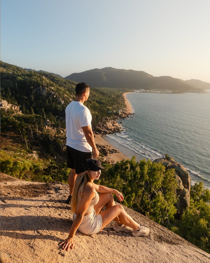 A couple rest on a hike in Townsville, looking out over the ocean.