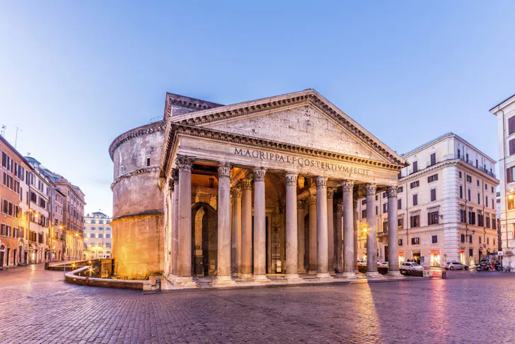 The Pantheon in Rome at dusk with its grand columned portico, ancient stone facade and cobblestone piazza glowing under soft evening light
