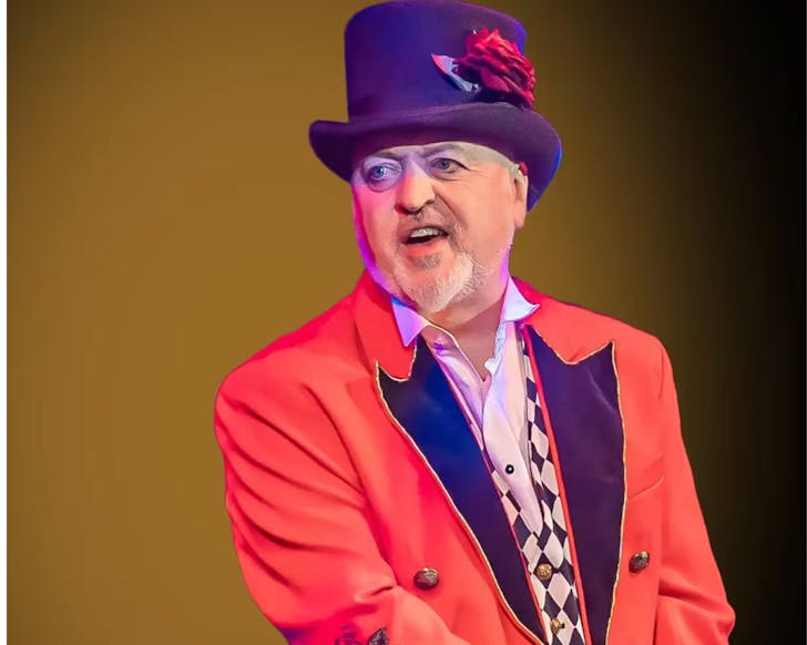 Bill Bailey in a bright orange and purple suit with a purple tophat and chequered waistcoat.