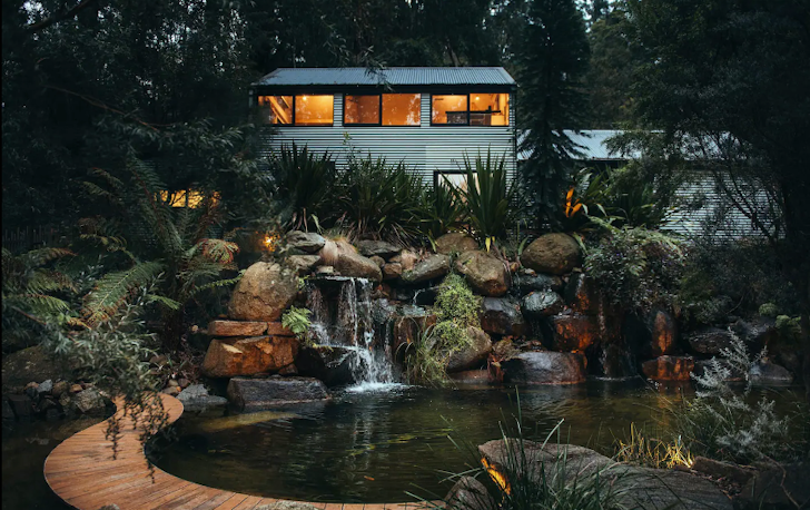 A house lit up at night with a rainforest in the background. 