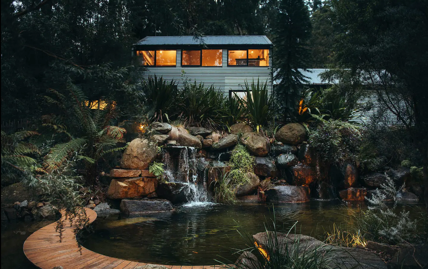 A house lit up at night with a rainforest in the background. 