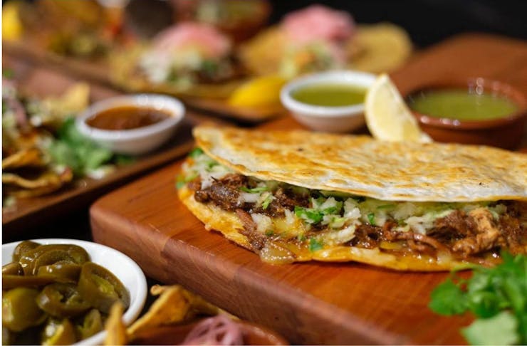 A close up shot of Birria tacos with meat, molten cheese and toppings.