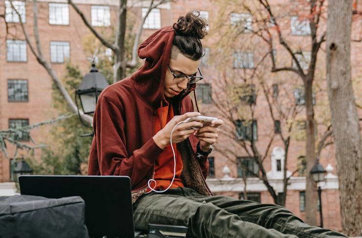 A man in a hoodie sitting using his phone in an urban area