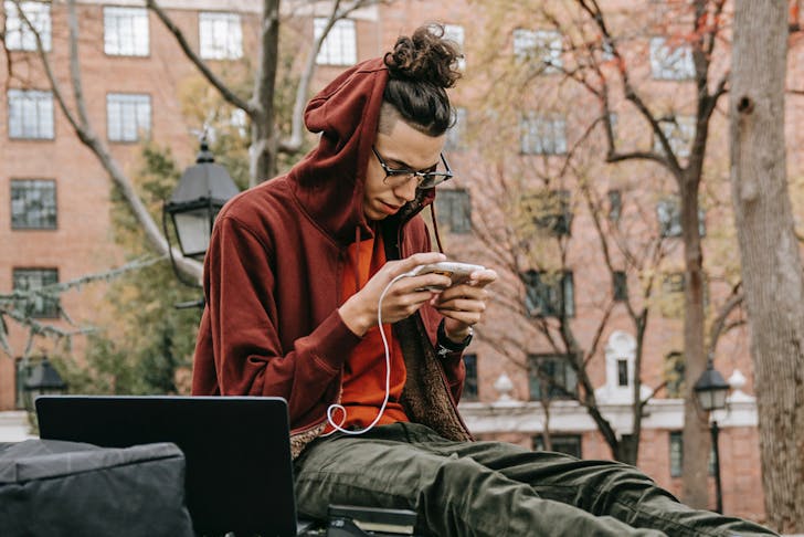 A man in a hoodie sitting using his phone in an urban area