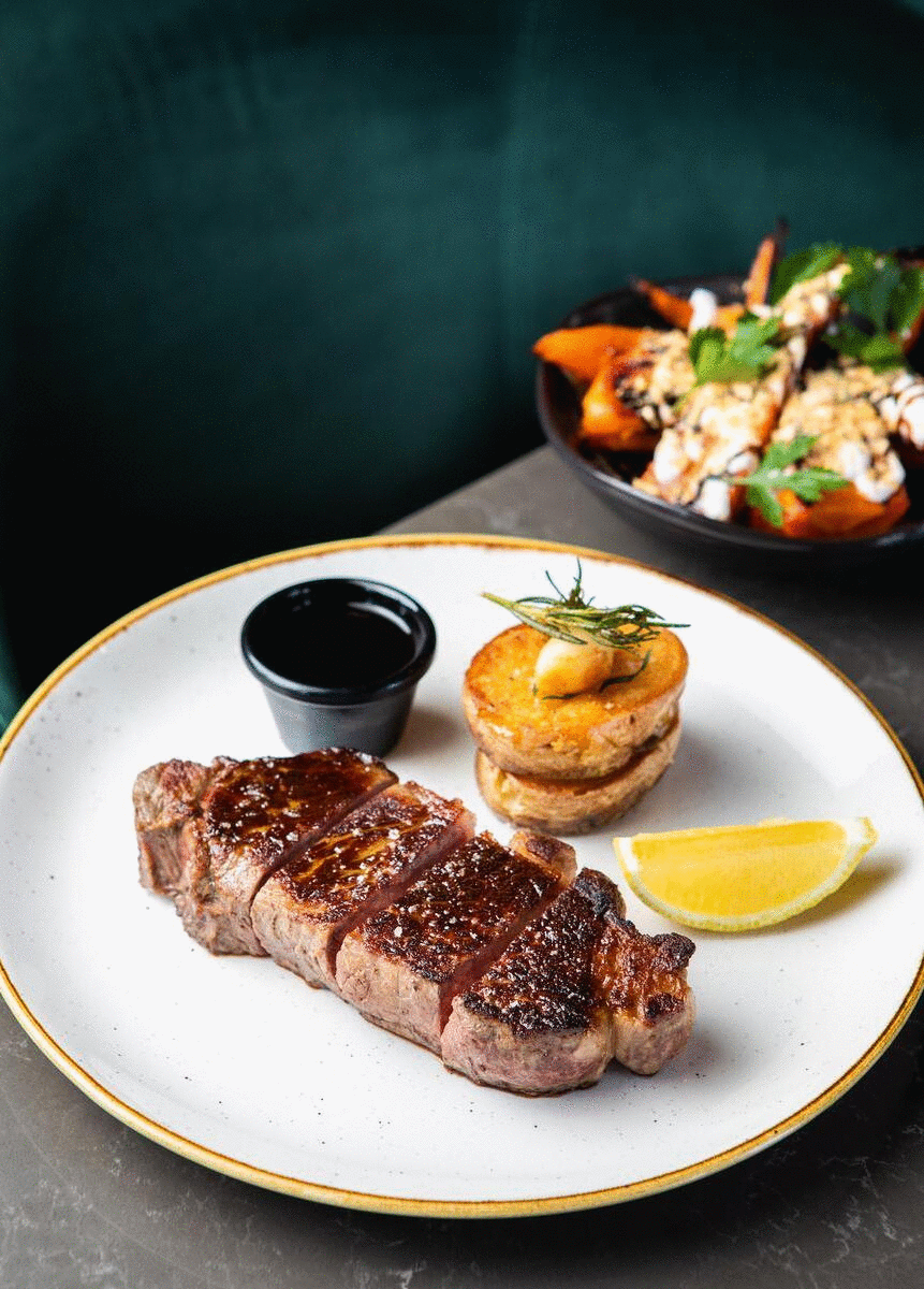 A juicy steak and bowl of carrots sit atop a wooden table.