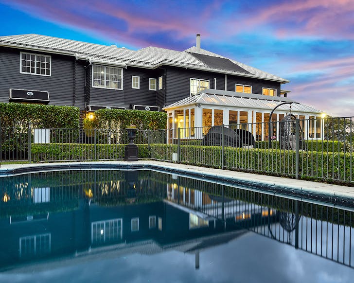 A black mansion with large pool, lawn and hanging egg chair against a stunning blue and purple sky. 