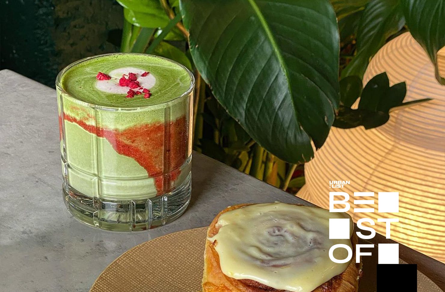 A glass of strawberry matcha beside a sticky bun.