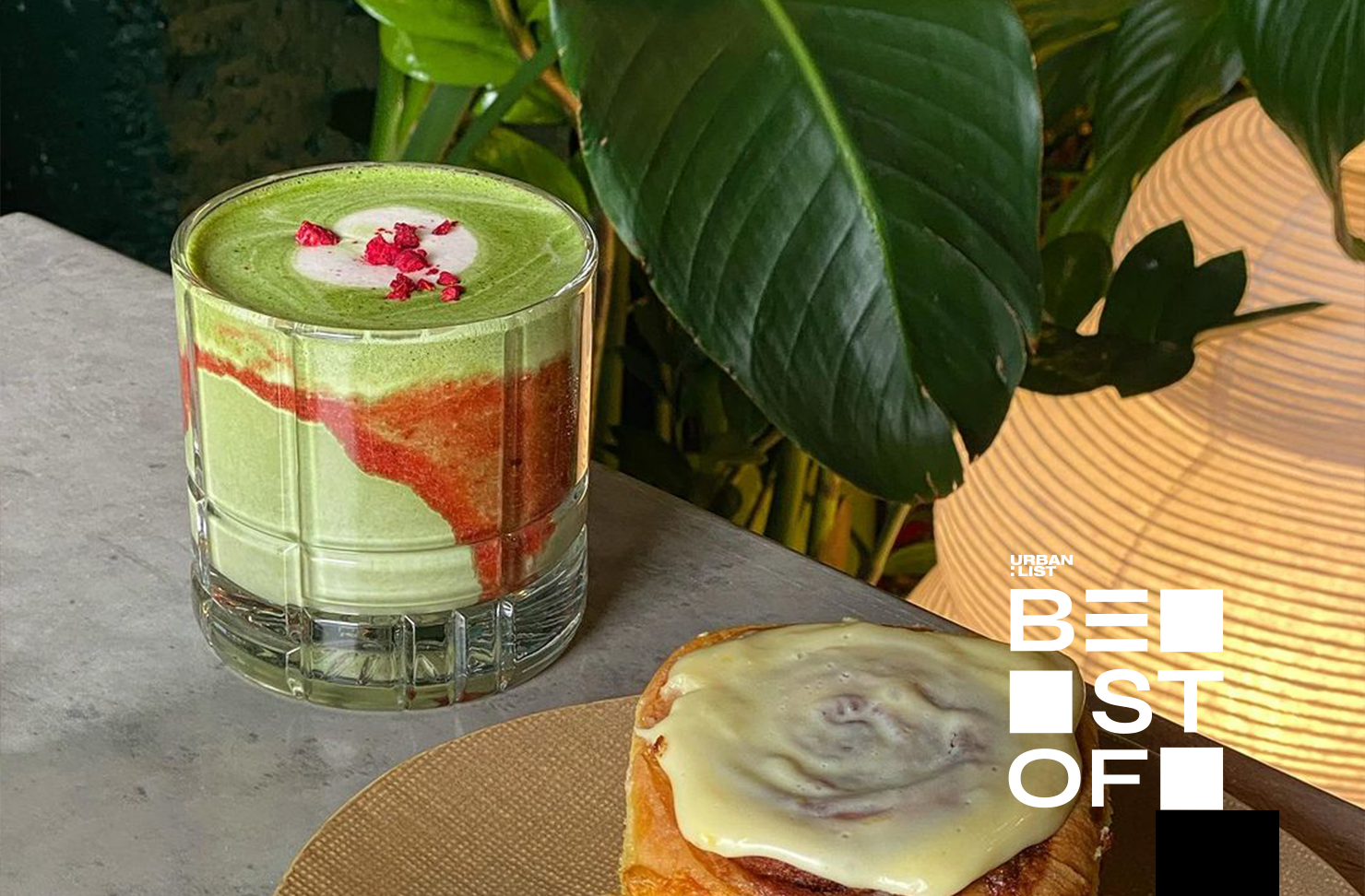 A glass of strawberry matcha beside a sticky bun.
