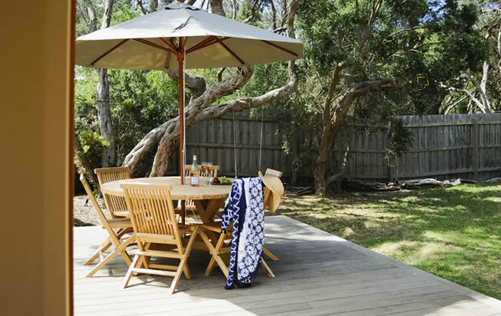 An outdoor deck with a table and umbrella and backyard. 