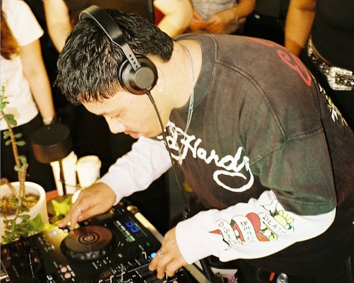 A closeup of a man leaning over a DJ set as he plays tunes.